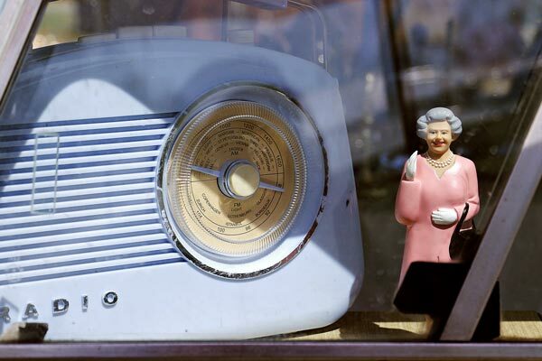 Königin Elisabeth II als Plastikfigur, winkend, steht neben einem alten Radio