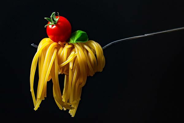 Spaghette auf einer Gabel, darauf eine kleine Tomate und ein Basilikumblatt