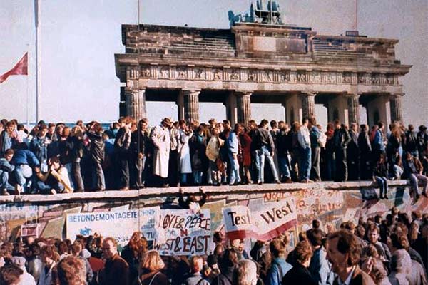 Menschen stehen auf der Berliner Mauer, im Hintergrund das Brandenburger Tor