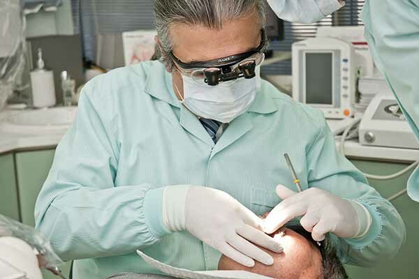 Zahnarzt mit Mundschutz, Kittel und Handschuhen, untersucht den Mund eines Patienten