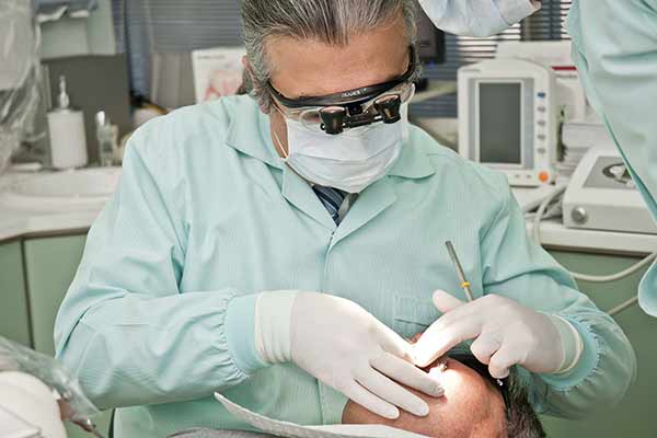 Zahnarzt mit Mundschutz, Kittel und Handschuhen, untersucht den Mund eines Patienten