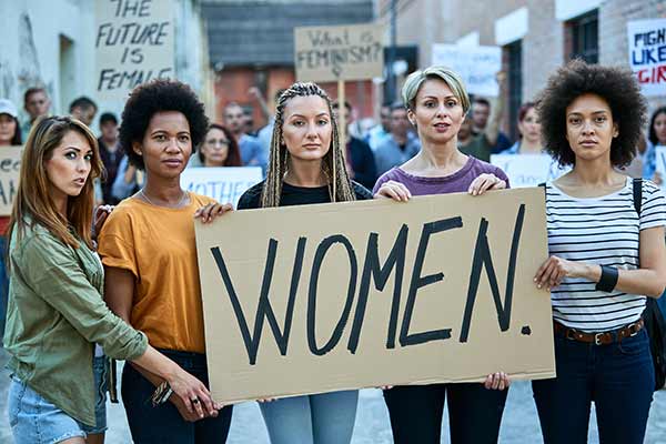 Frauen auf einer Demonstration. Fünf Frauen halten ein Schild mit der Aufschrift "Women".