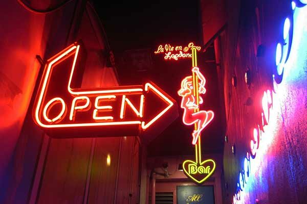 Eingang einer Bar mit Neonbuchstaben "Open", daneben eine stilisierte Pole-Dancerin