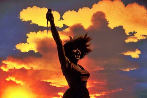 Tina Turner als Silhouette vor einem Sonnenuntergang. Sie streckt den Arm nach oben, sie singt und ihr Haar weht im Wind