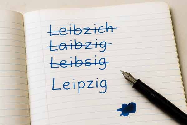 Schulheft - das Wort Leipzig mit blauer Tinte dreimal falsch geschrieben und durchgestrichen, darunter die korrekte Schreibweise